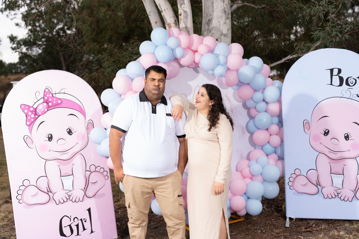 Couple poses by pink and blue balloon arch with baby-themed backdrop panels.