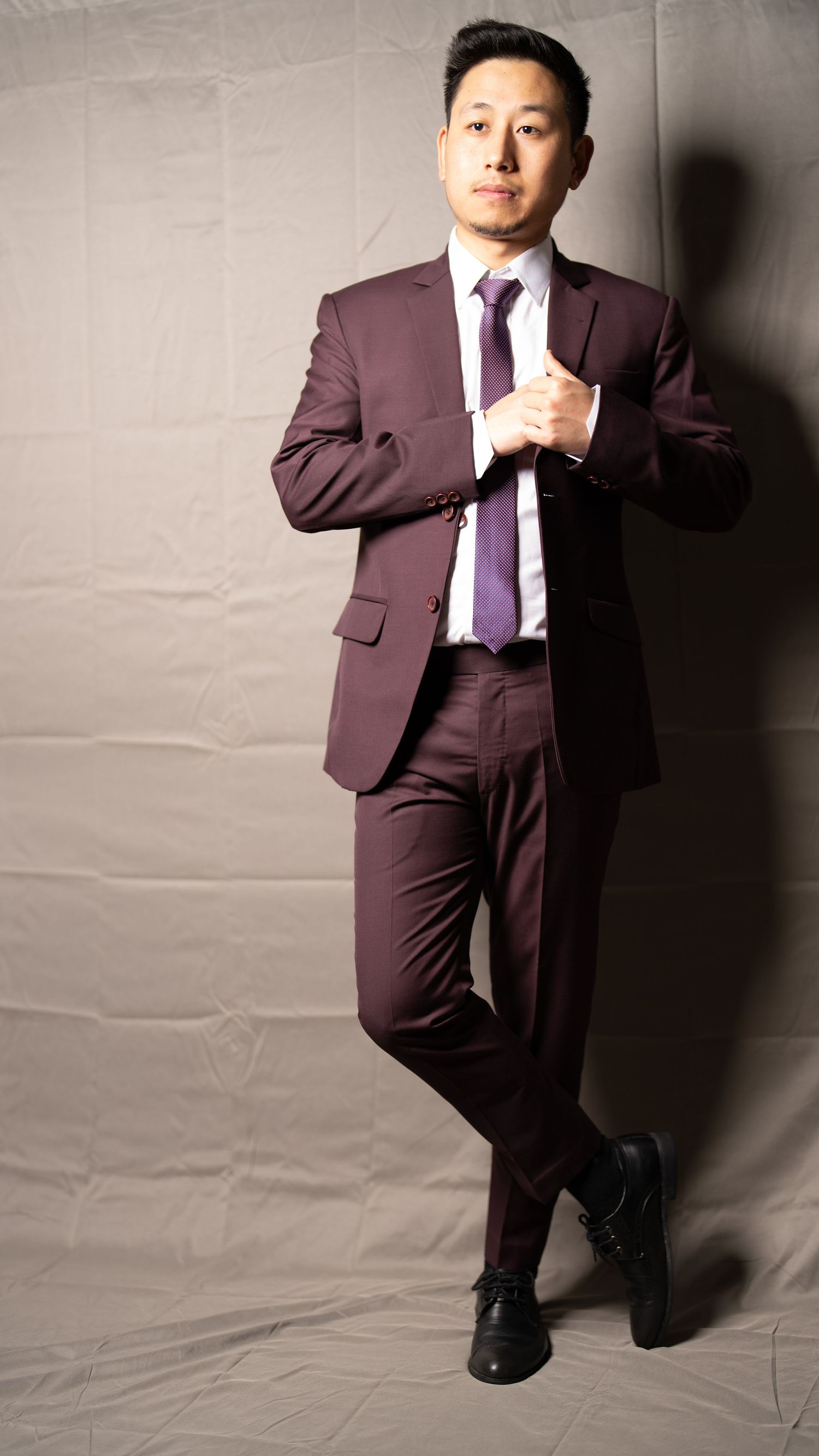 Professional photoshoot of person in burgundy suit striking dynamic poses against grey backdrop.