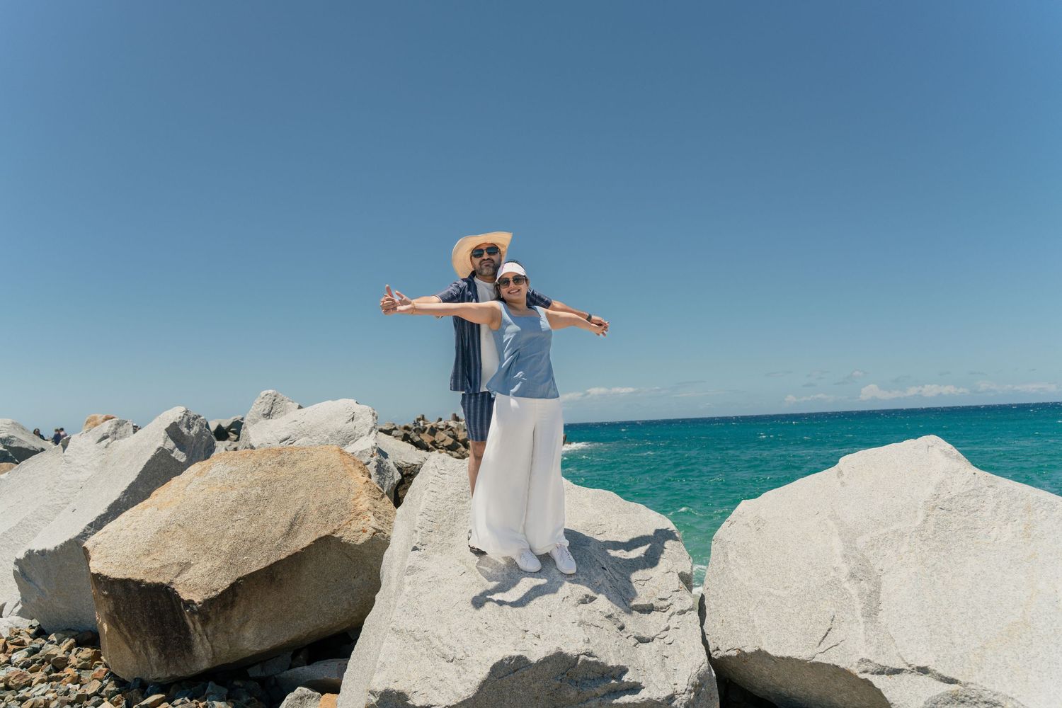 Person in white poses gracefully on large white coastal rocks with turquoise ocean in background.