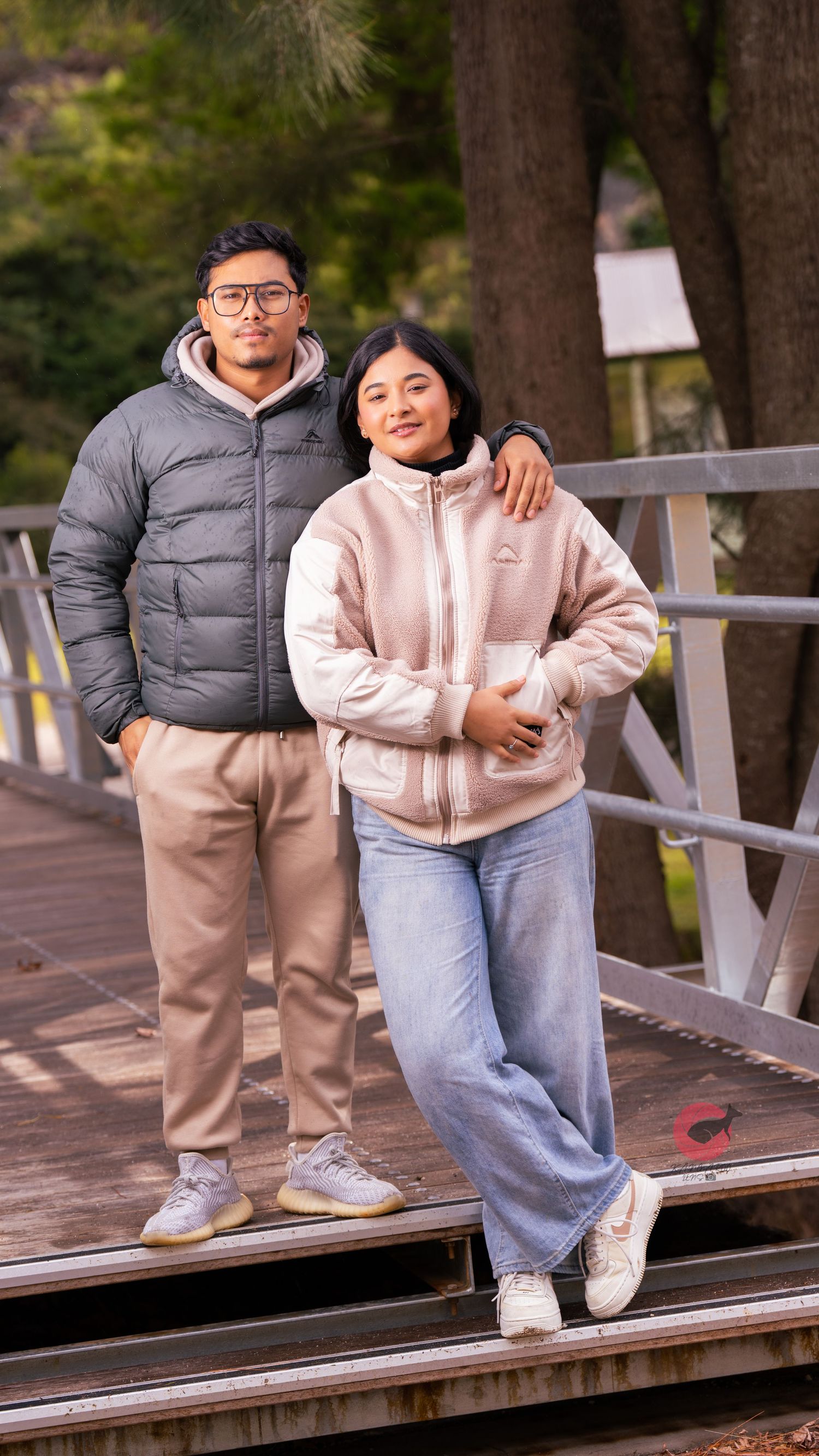 Couple in cozy winter outfits poses together on wooden boardwalk during autumn.
