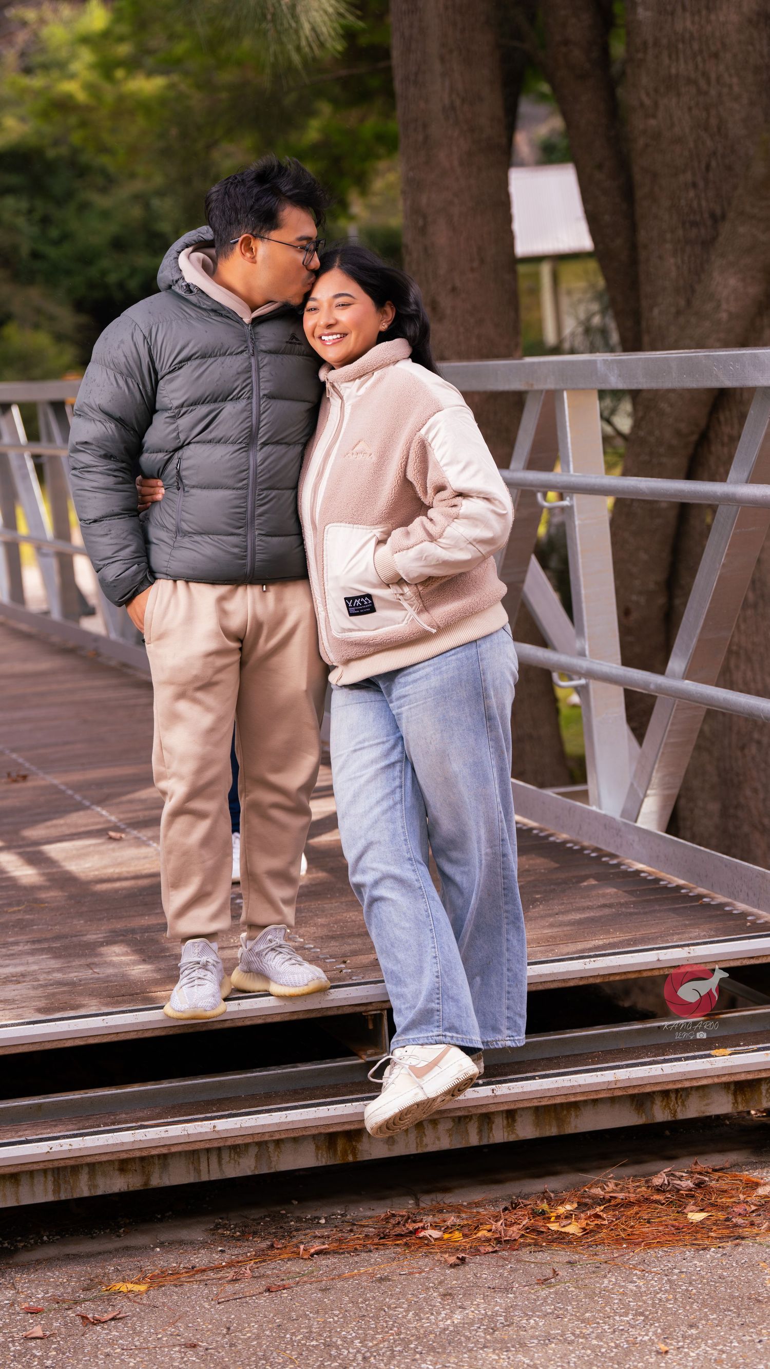 Two people in casual winter wear share affectionate moment on wooden walkway.