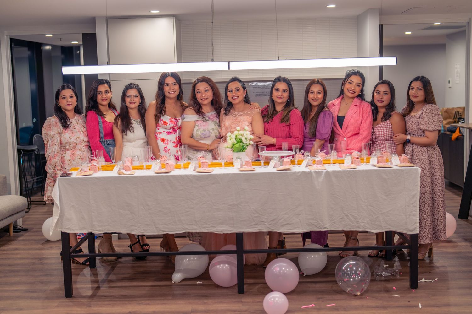 Group gathered around long table with pink decorations and refreshments for a celebration.