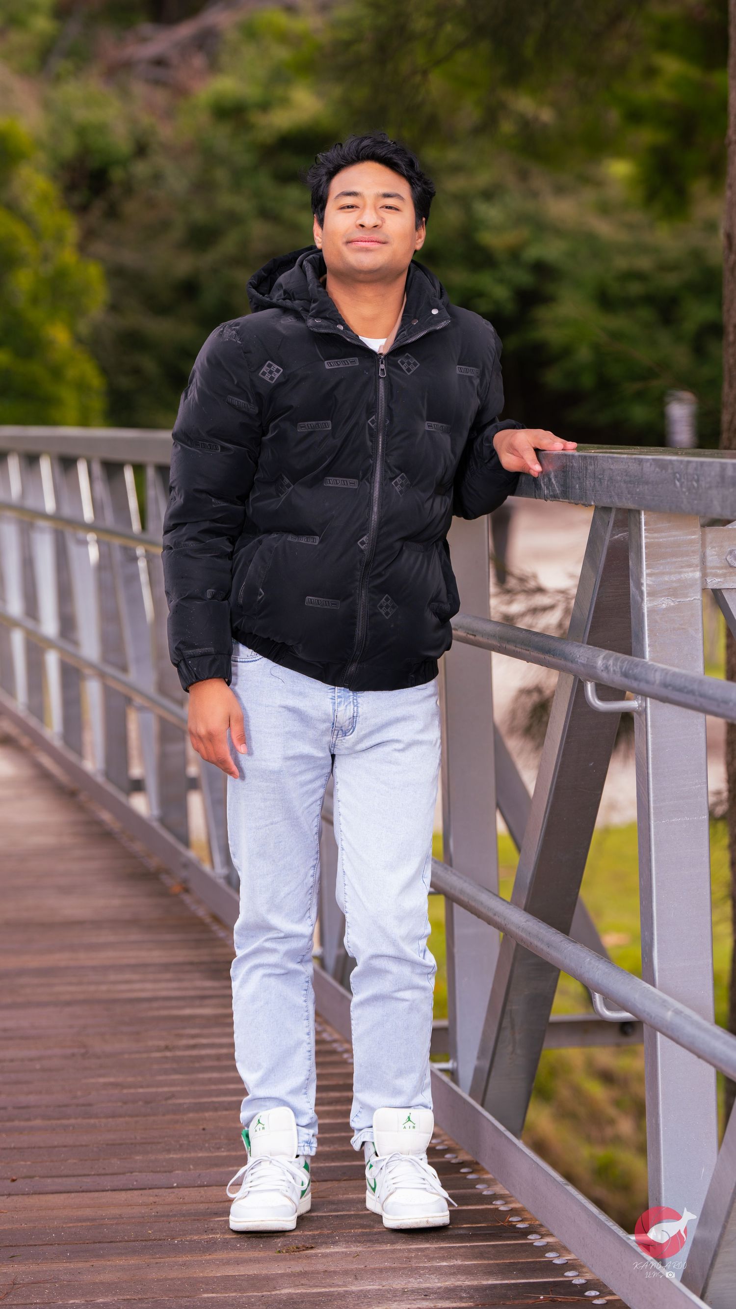 Person in black puffer jacket and light jeans poses casually on wooden bridge walkway.