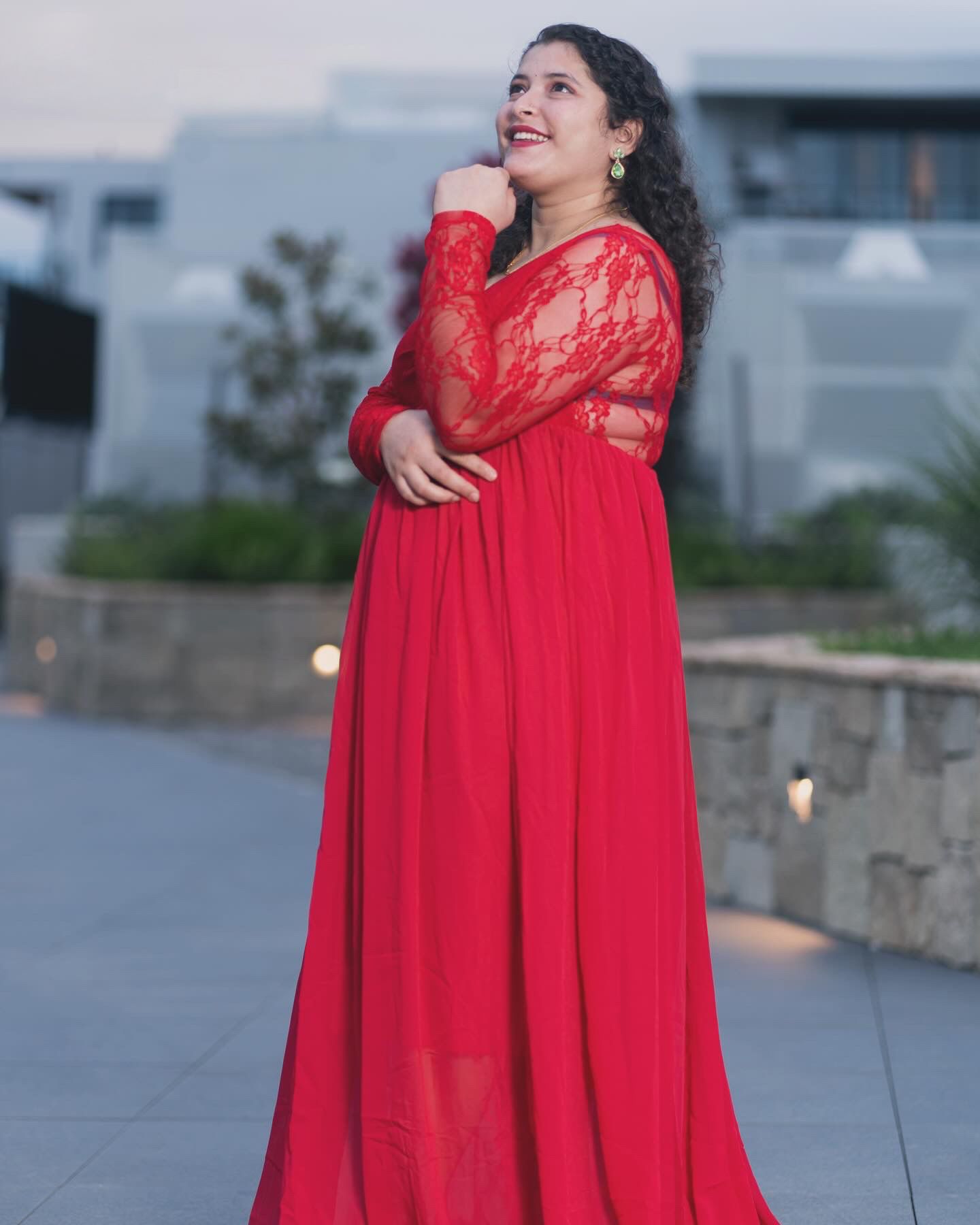 Fashion portrait series in a flowing red dress against an urban backdrop at dusk.