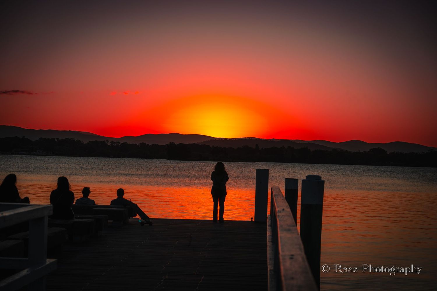 Dramatic sunset silhouettes of people standing by a dock over water.