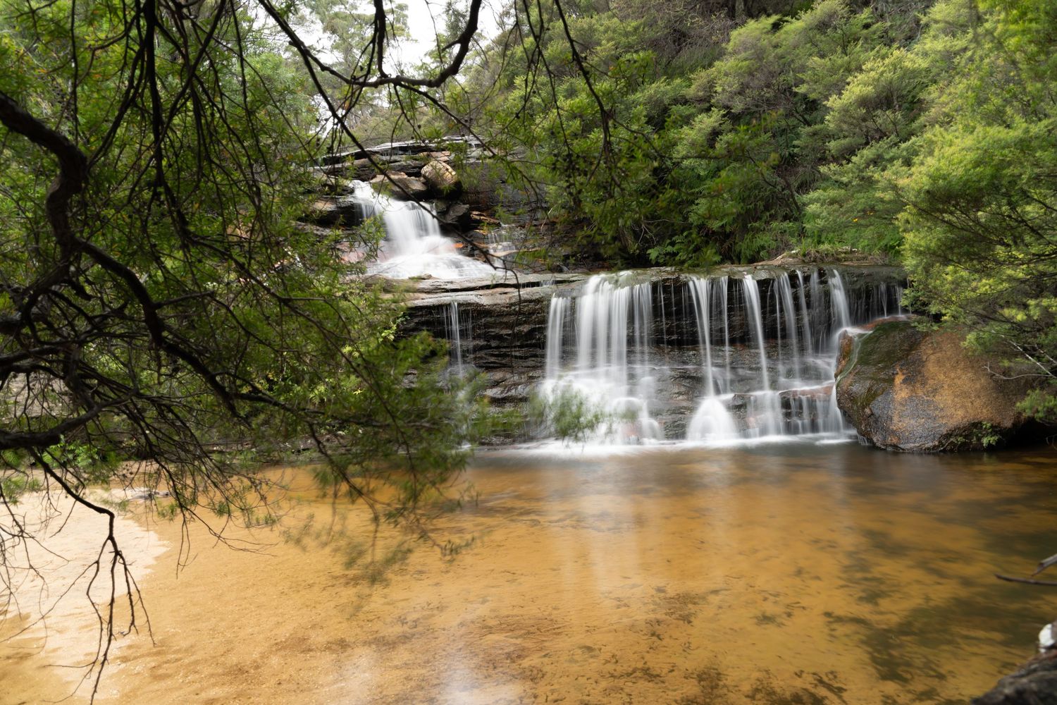 Cascading waterfalls flowing over rocky ledges in a lush green forest setting.