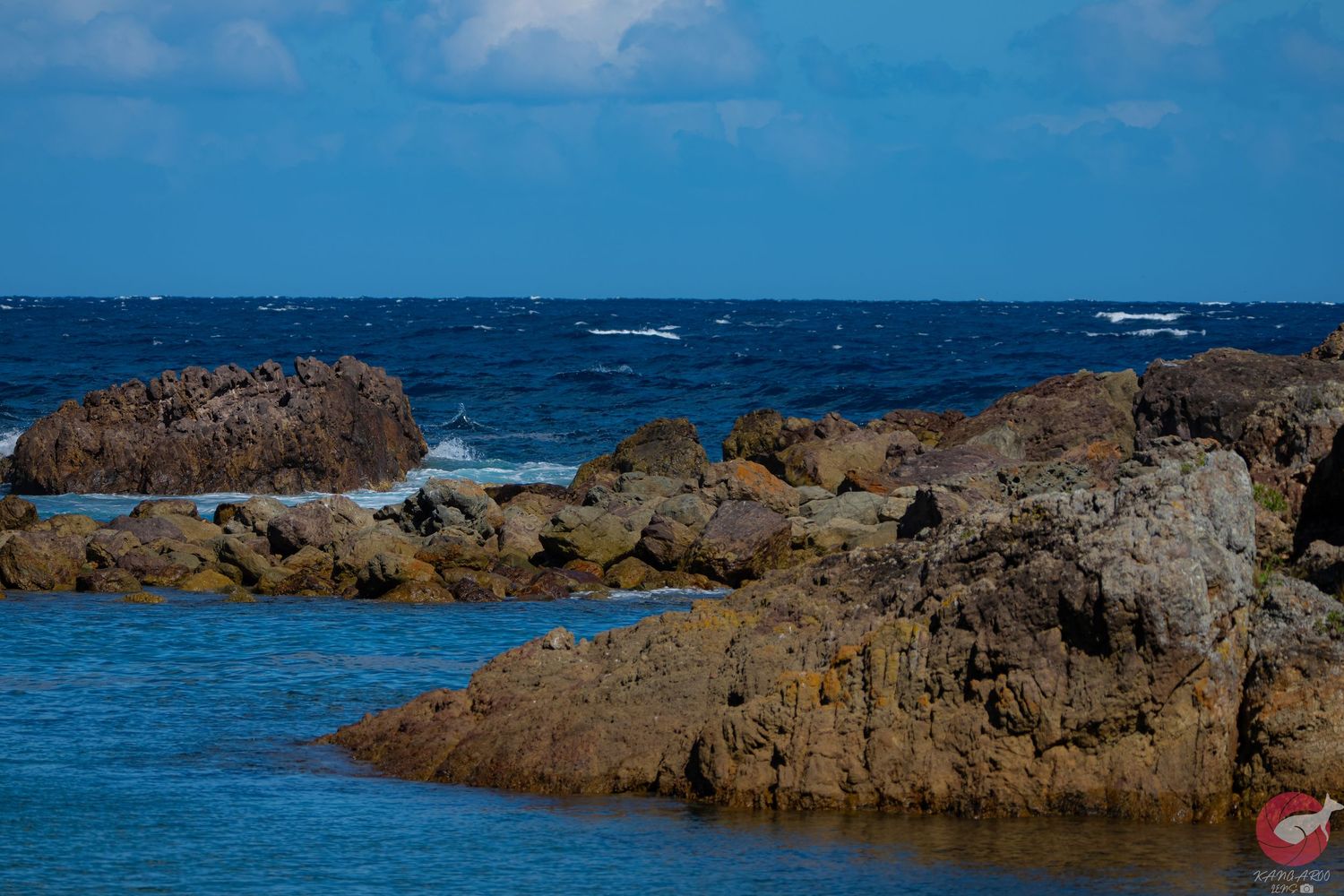 Rocky outcrops emerge from deep blue ocean waters under bright sky.