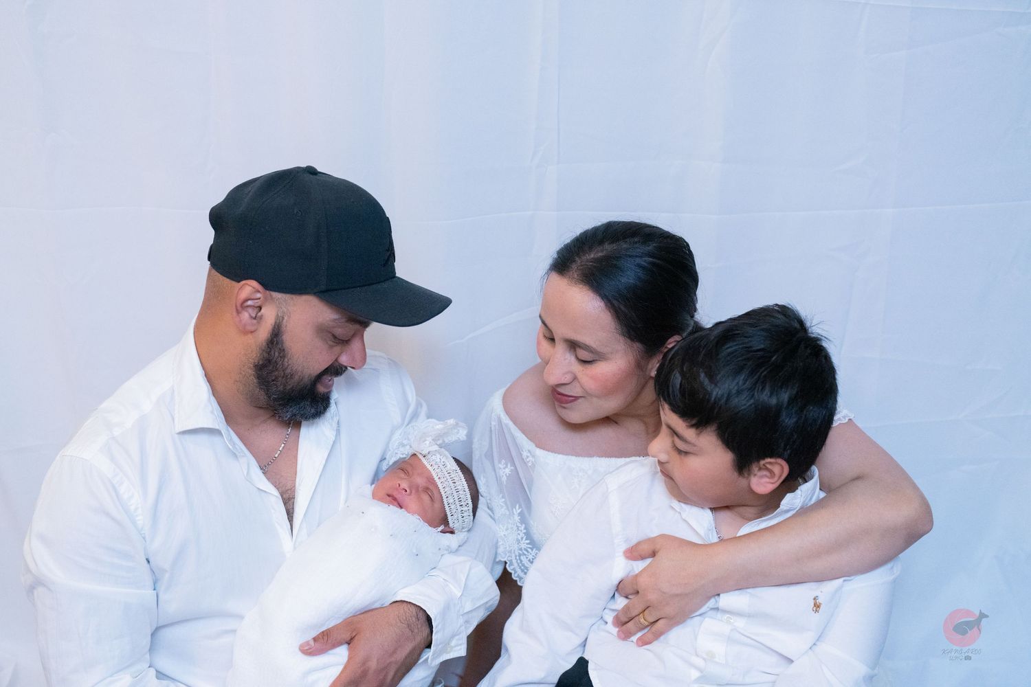 Family of four shares tender moment against white backdrop in matching outfits.