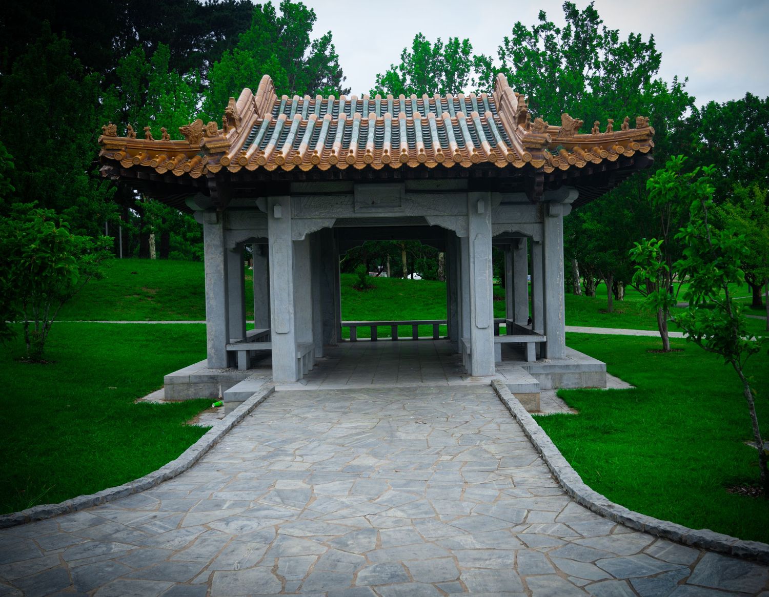Traditional Asian pavilion with stone courtyard surrounded by lush green gardens.