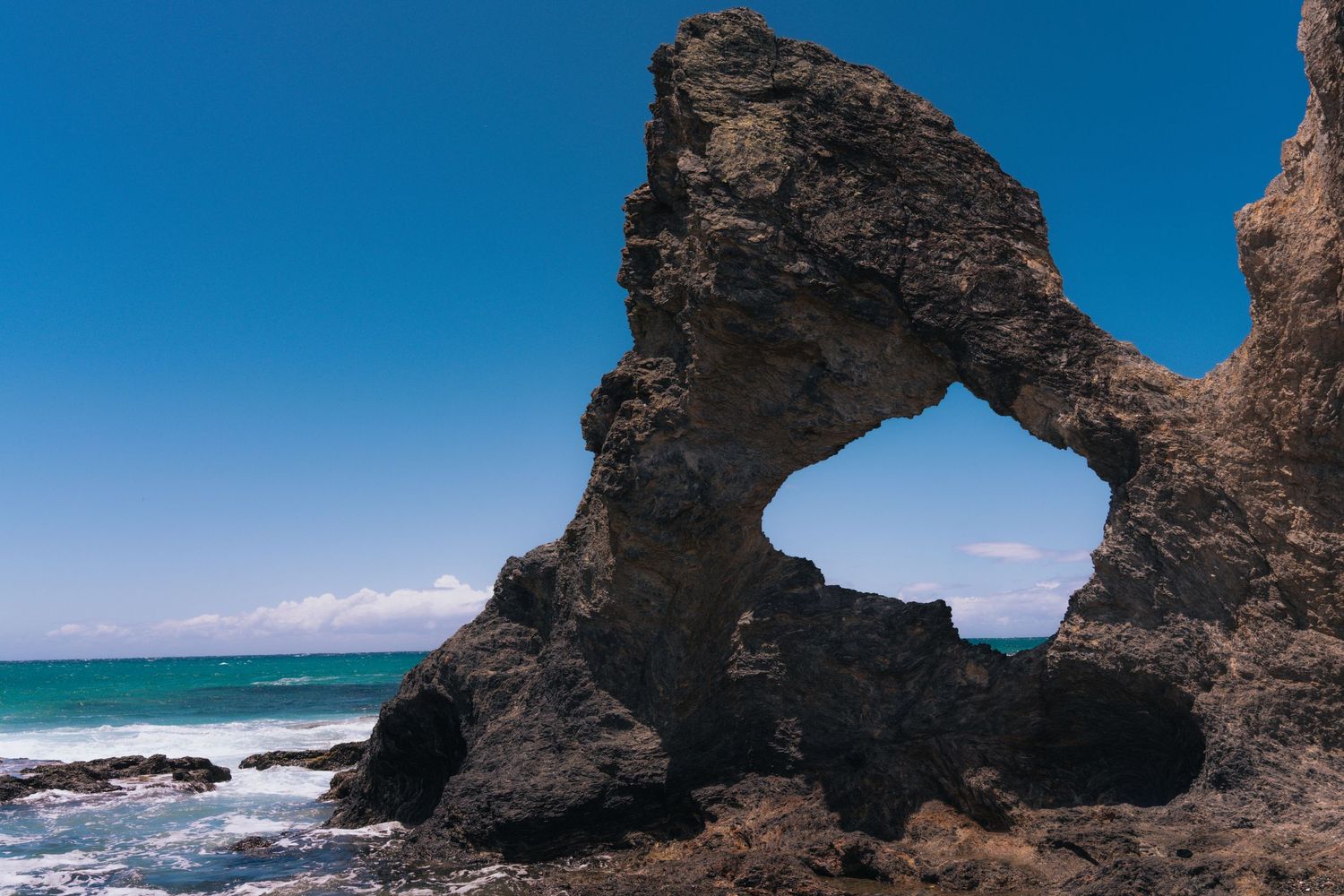 Rocky coastal formations and natural arches frame the turquoise ocean waters.