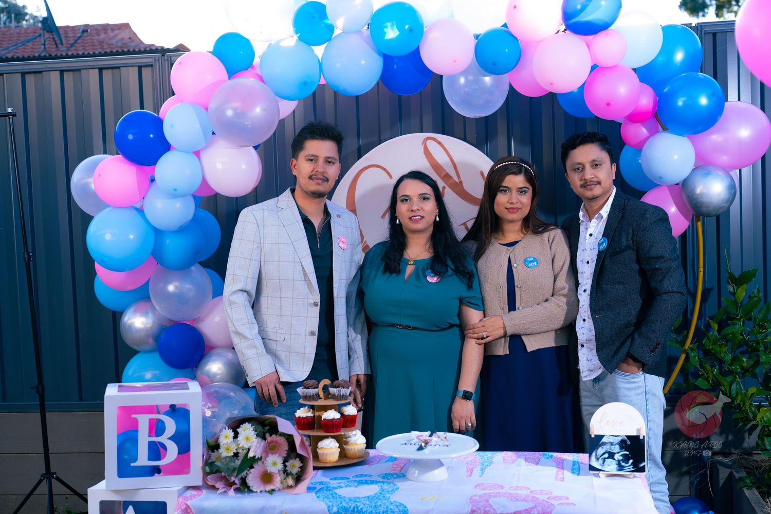 Small group poses by blue and pink balloon arch at gender reveal party.