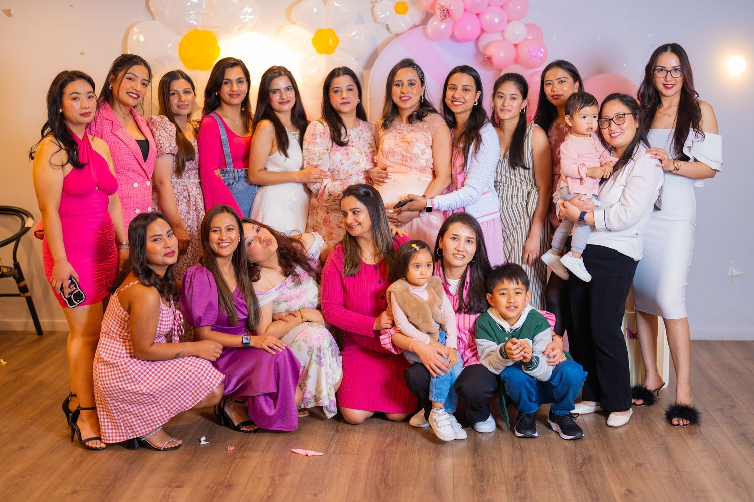 Celebration group photo with people wearing pink and white outfits against balloon backdrop.