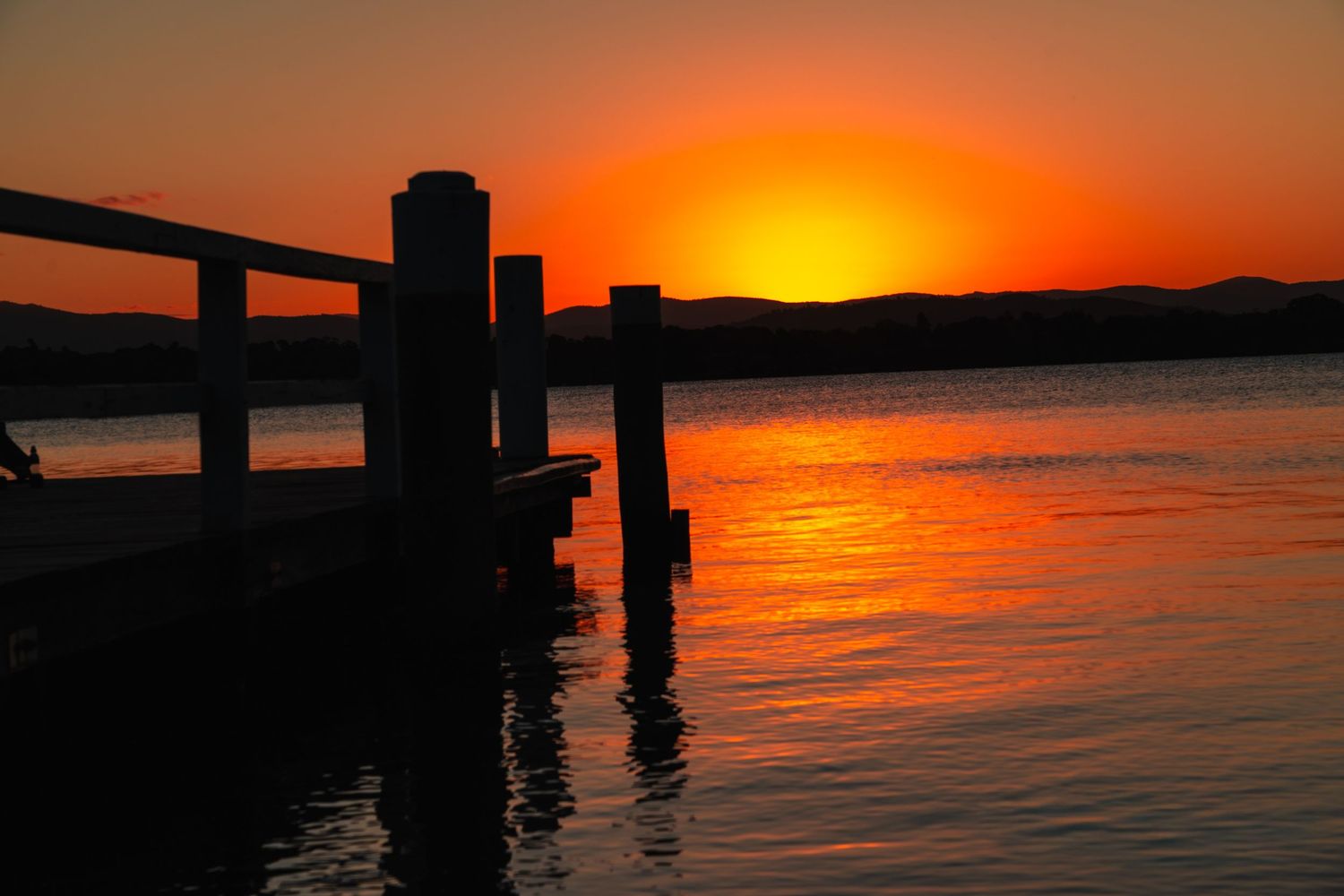 Vibrant orange sunset over water with silhouetted pier structures creating dramatic reflections.