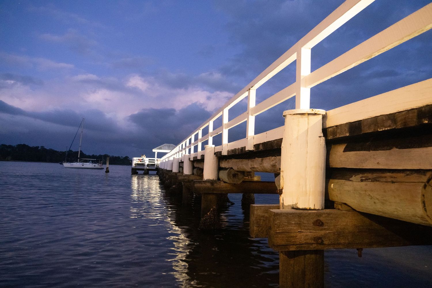 Wooden pier extends over calm waters under a moody blue sky.