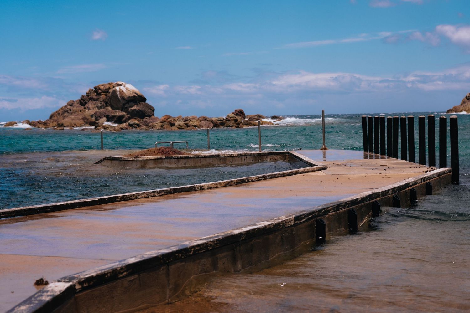 Oceanside pool platform with rocky headland and blue waters in the background.