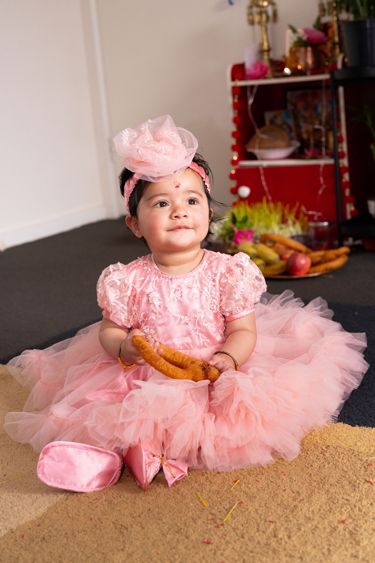 Baby in pink tulle dress and bow lying on beige carpet.