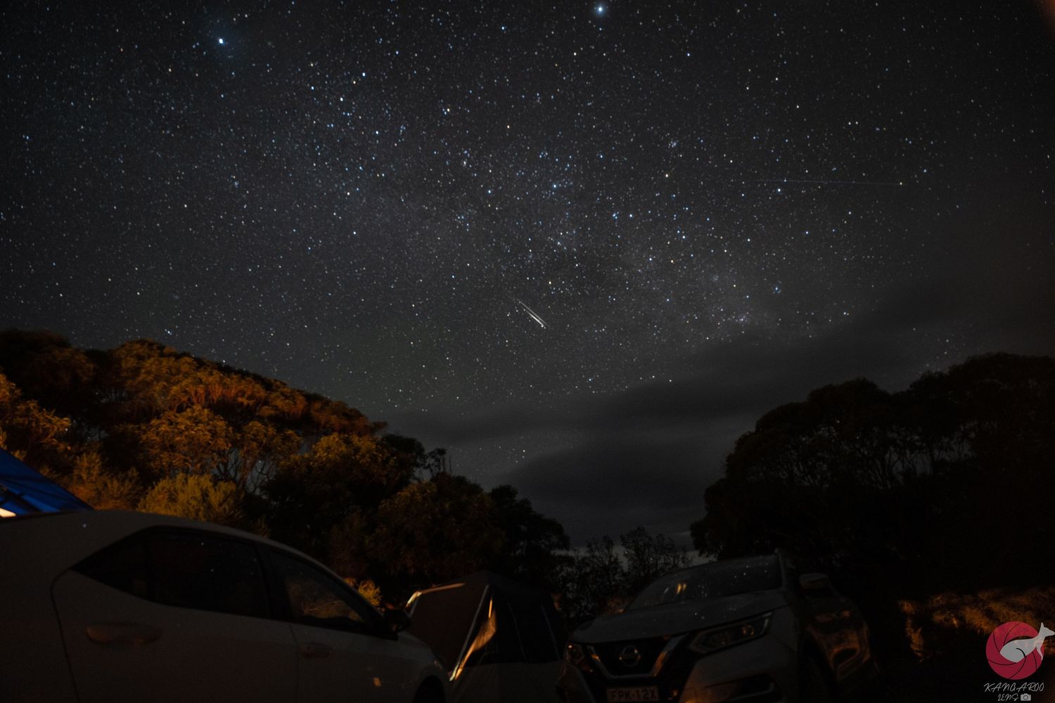 Long exposure night sky photograph showing star trails and silhouetted landscape.