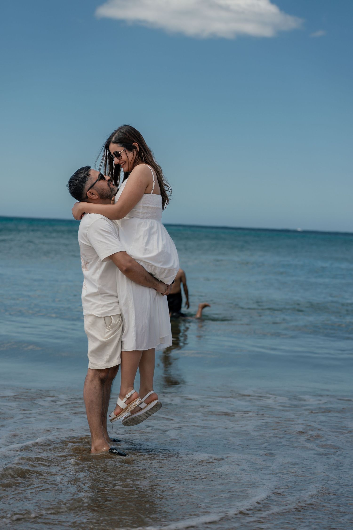 Couple shares romantic moment while standing in shallow ocean waters on sunny day.