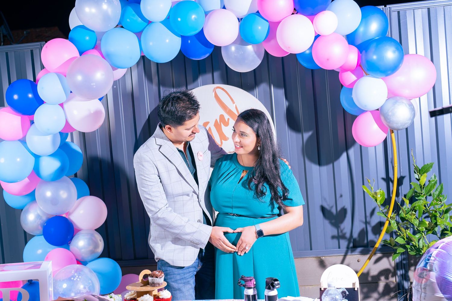 Festive celebration decorated with pink and blue balloon arch and white curtains in background.