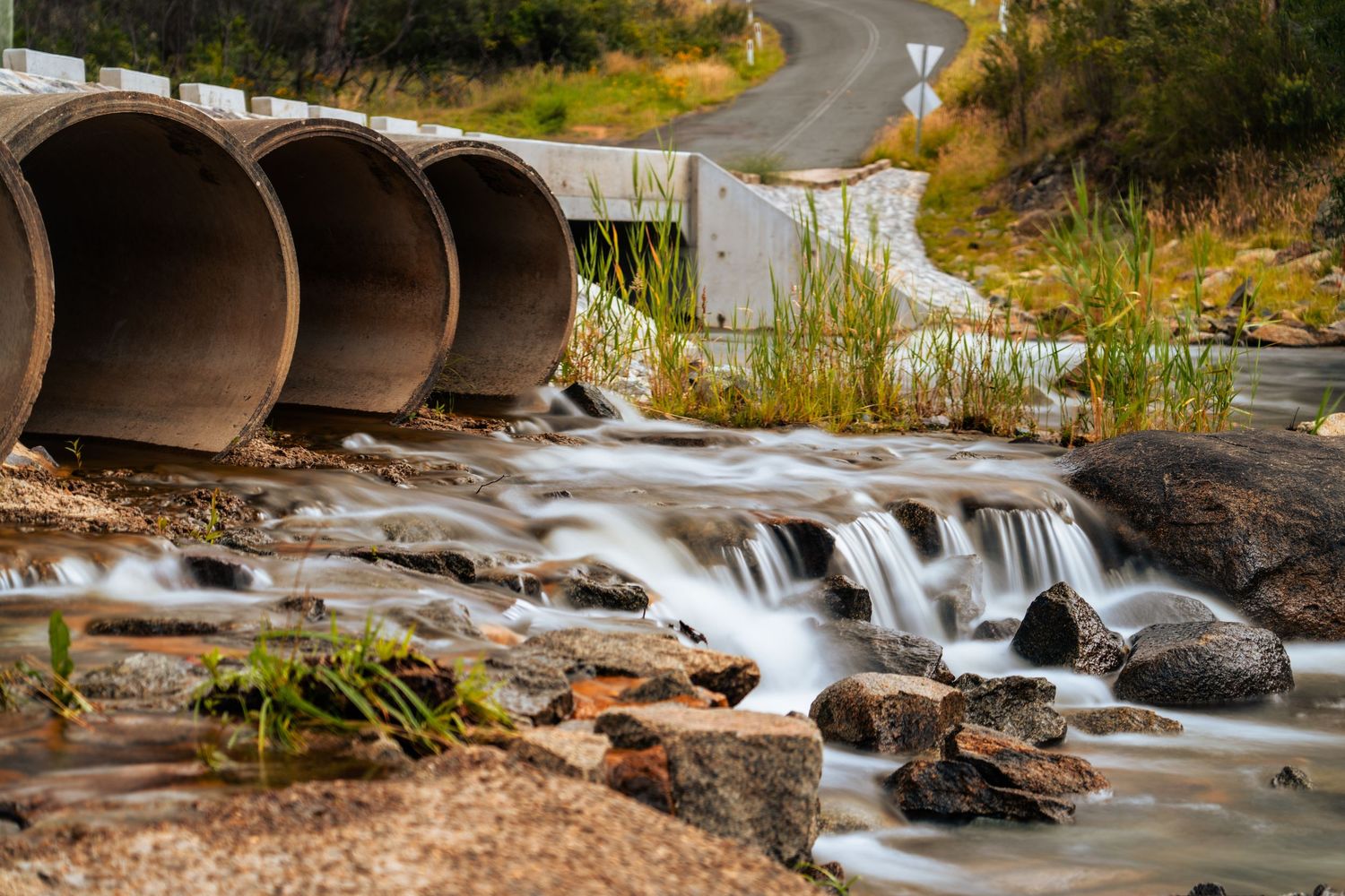 Water cascades over rocky terrain through drainage culverts in a natural setting.