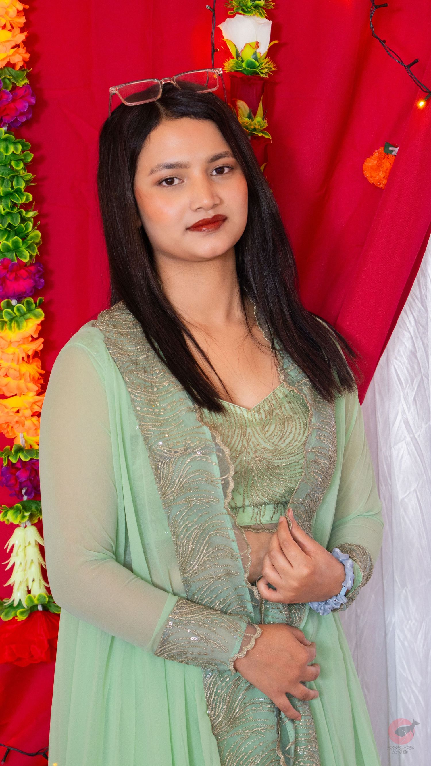 Portrait against red backdrop with floral decorations featuring person in mint green lace dress.