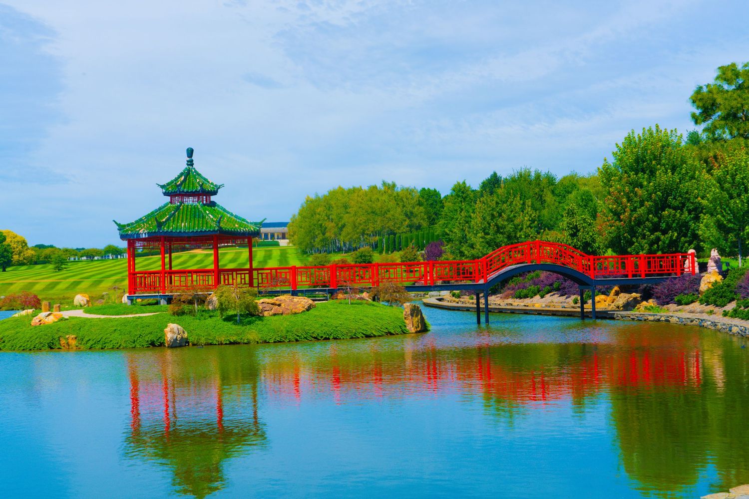 Scenic lakeside park with red pagodas and green landscaping reflecting on calm waters.