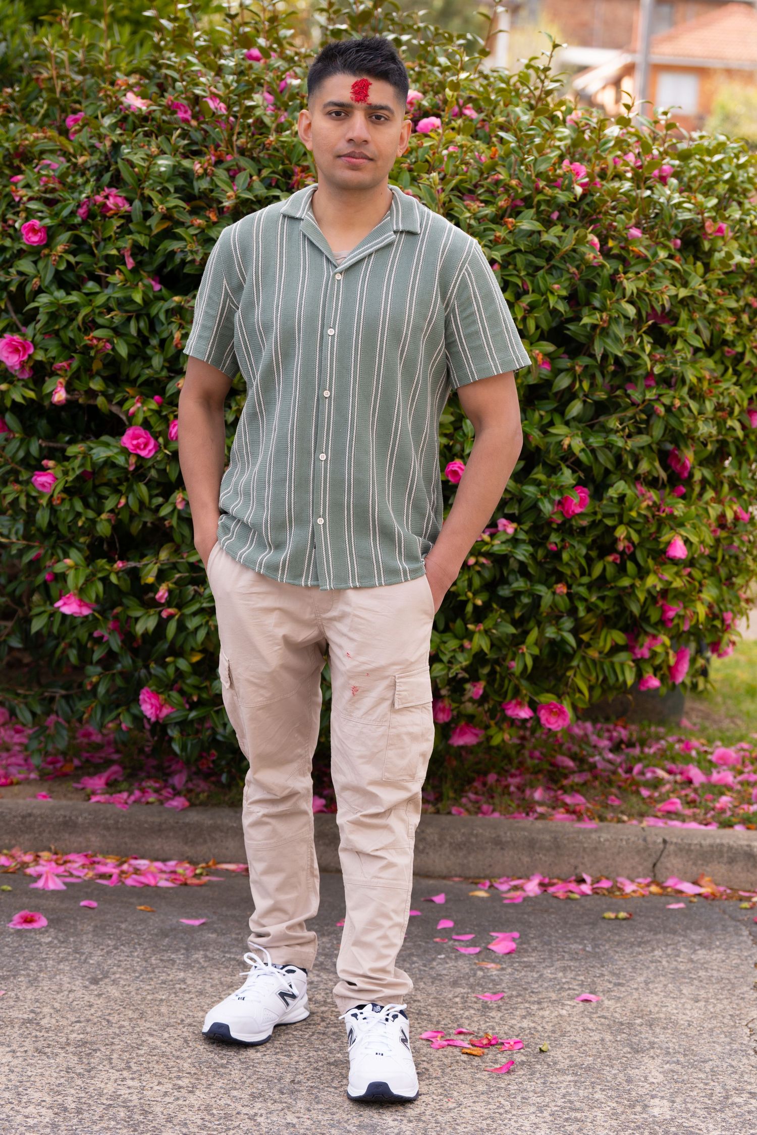 Person in striped shirt and khaki pants standing against flowering bush with pink blossoms.