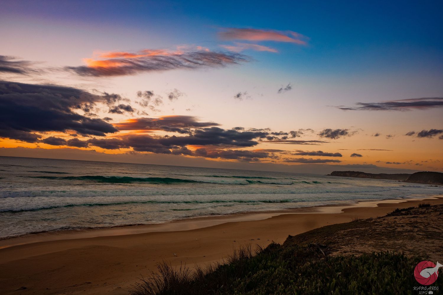 Coastal landscape at sunset with golden light illuminating the beach and rolling waves.