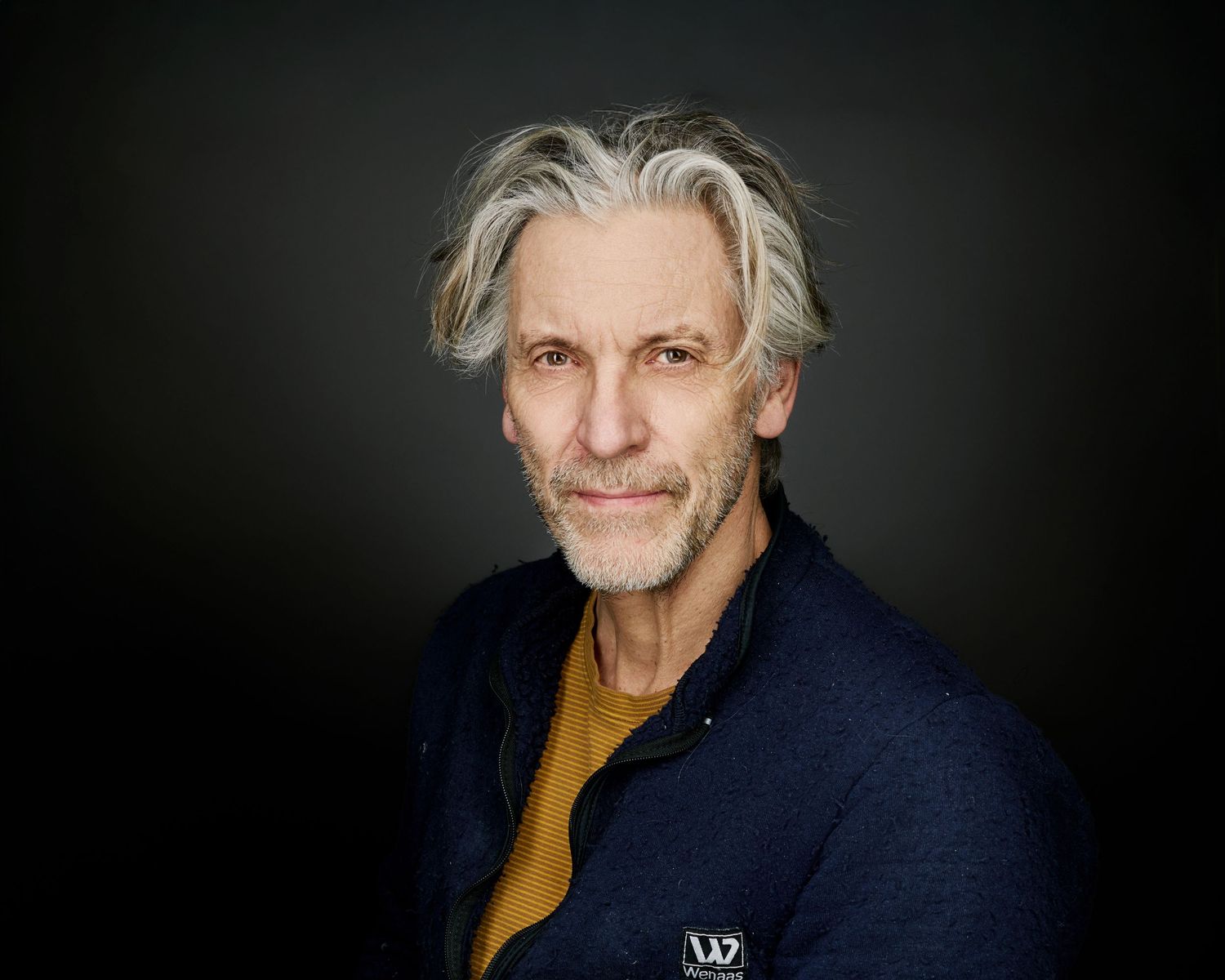 Professional headshot series showing someone in a navy blazer and gold shirt against a dark background.