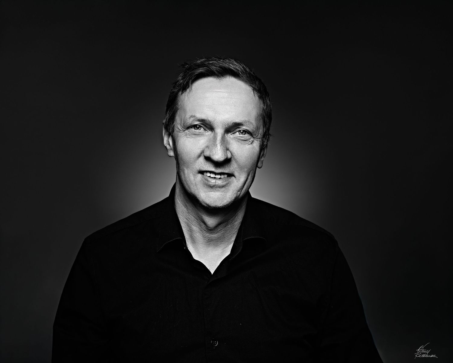 Black and white headshot portrait with dramatic lighting against dark background.