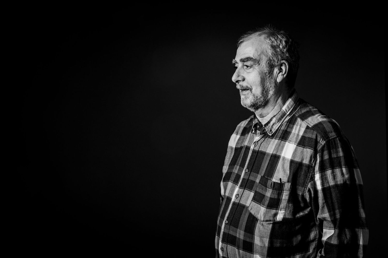 Black and white portrait of person wearing plaid shirt against dark background.