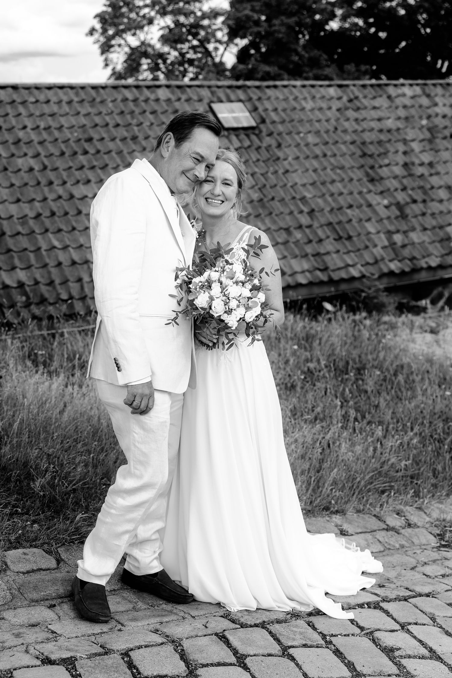 Wedding couple poses together on cobblestone path with rustic backdrop in black and white photography.