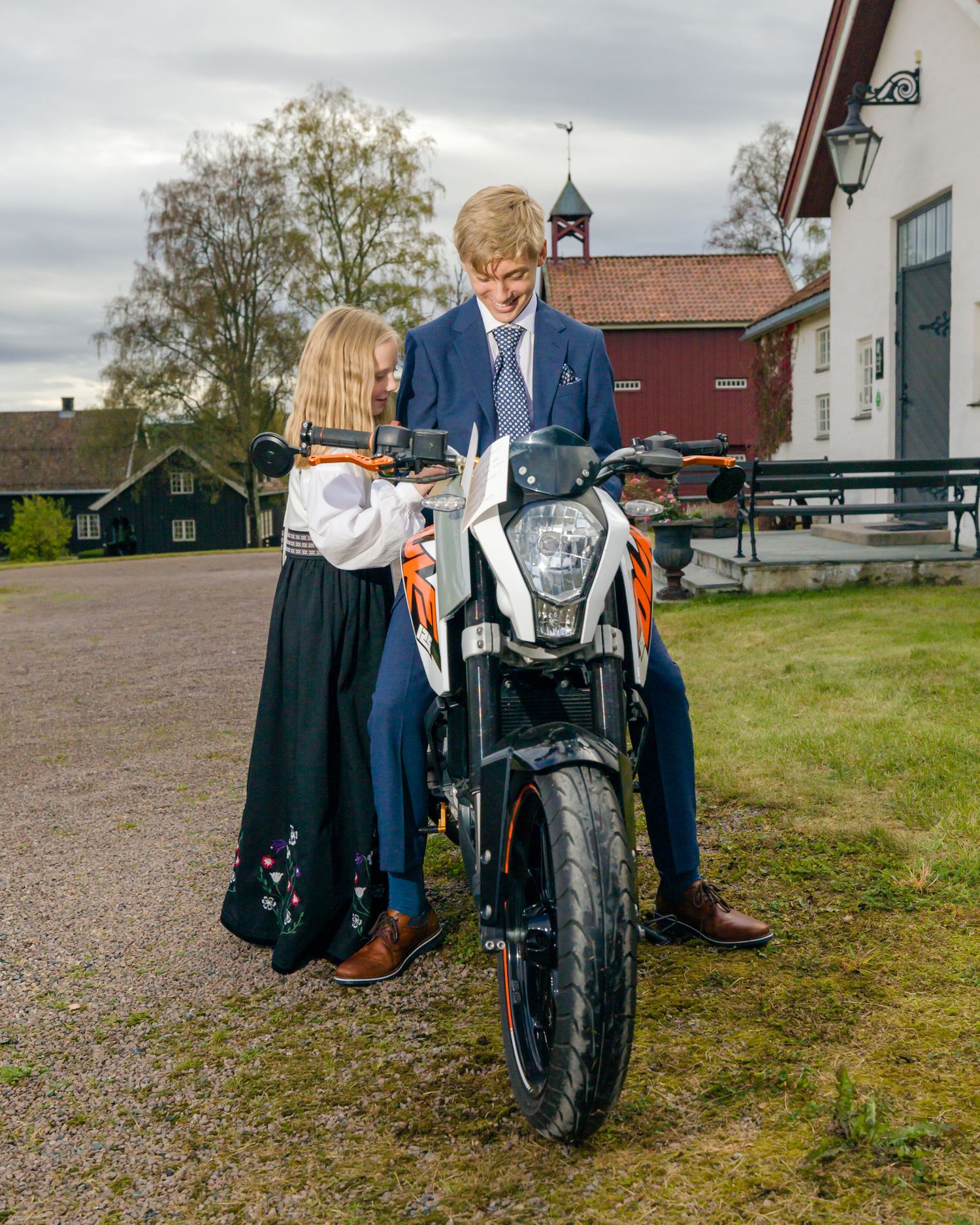 Konfirmant og slektning beundrer motorsykkel under konfirmasjonsfoto i Nittedal.