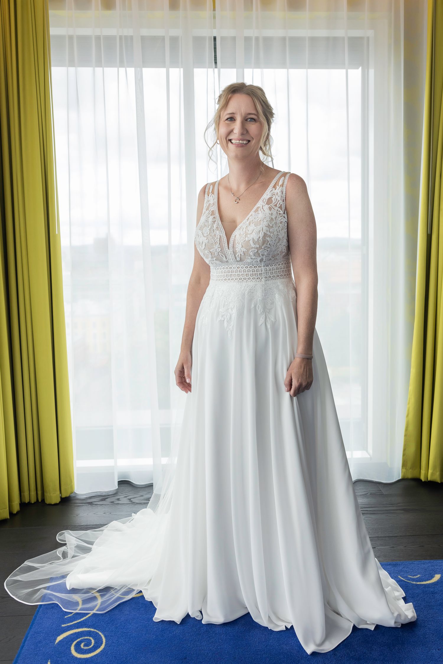 A flowing white wedding dress displayed on a blue floor with lime green curtains in the background.