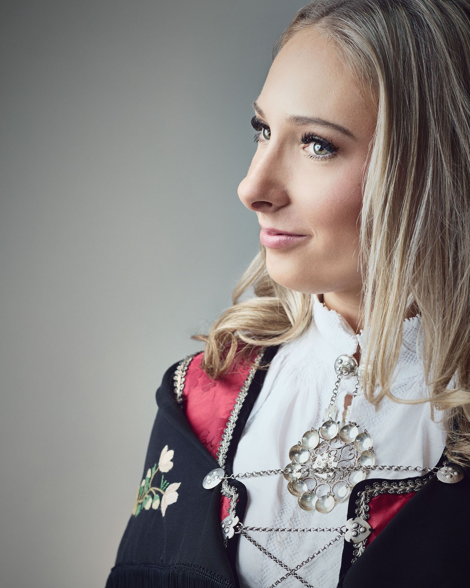Profile portrait of person in traditional dress with embroidered details and blonde hair.