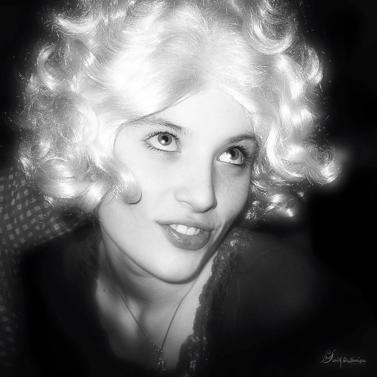 A glamorous black and white portrait shows a woman with platinum blonde curls and bright lipstick against a dark background.