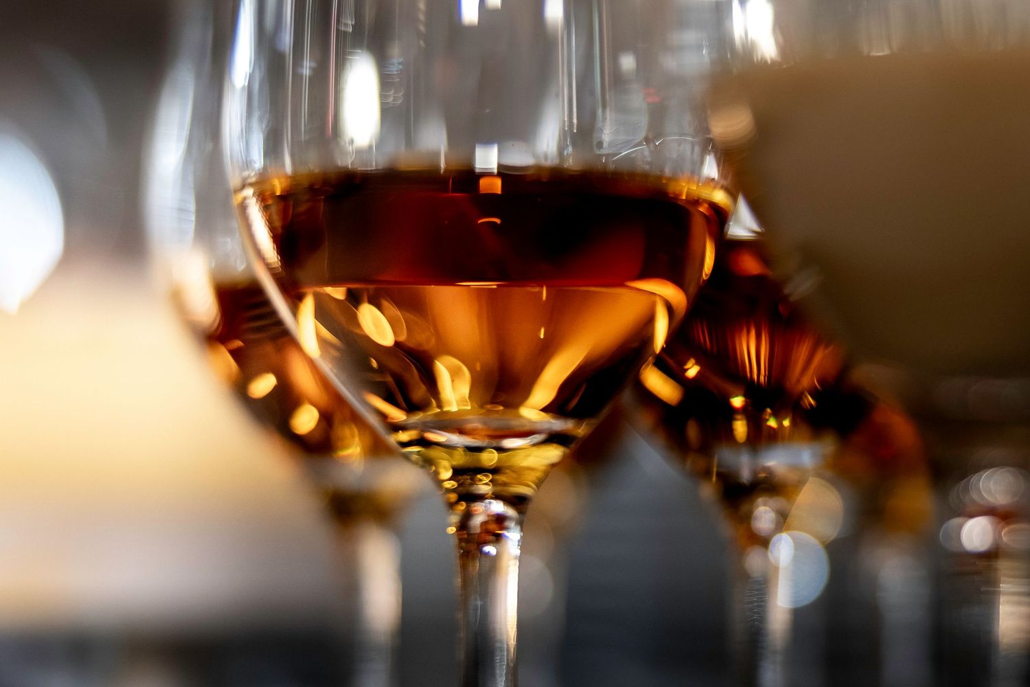 Row of elegant wine glasses filled with golden liquid in warm lighting.