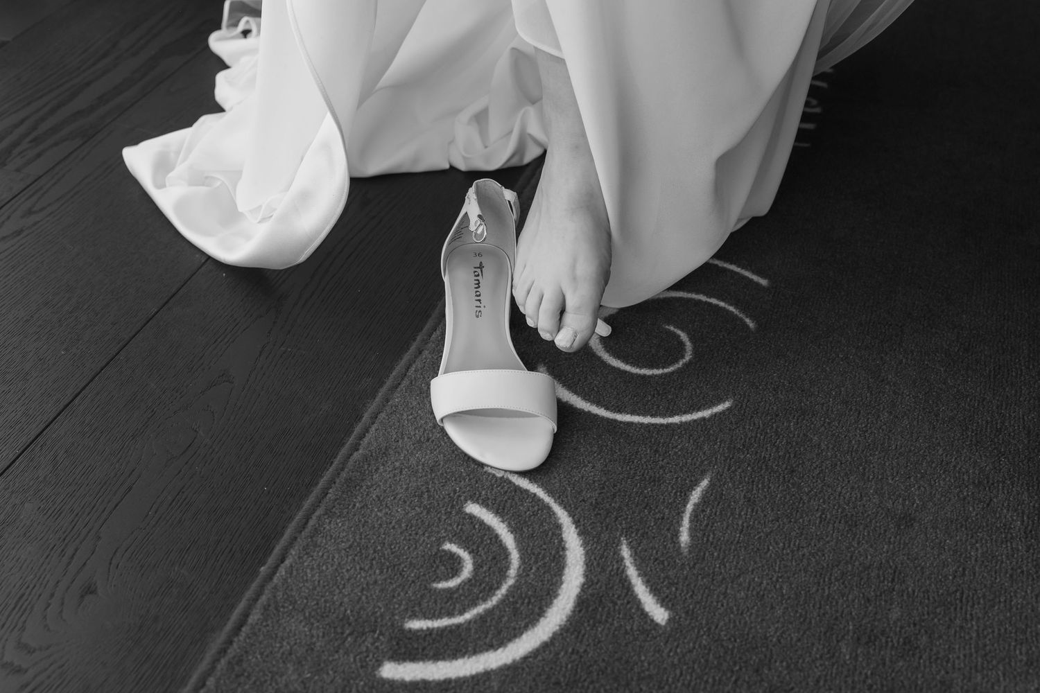 Black and white photo of a bride's foot with white high heel sandal next to decorative chalk markings on the floor.
