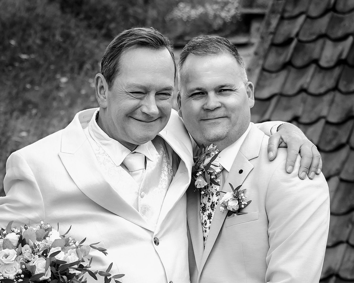 Black and white portrait of a couple in matching white attire with floral bouquet.