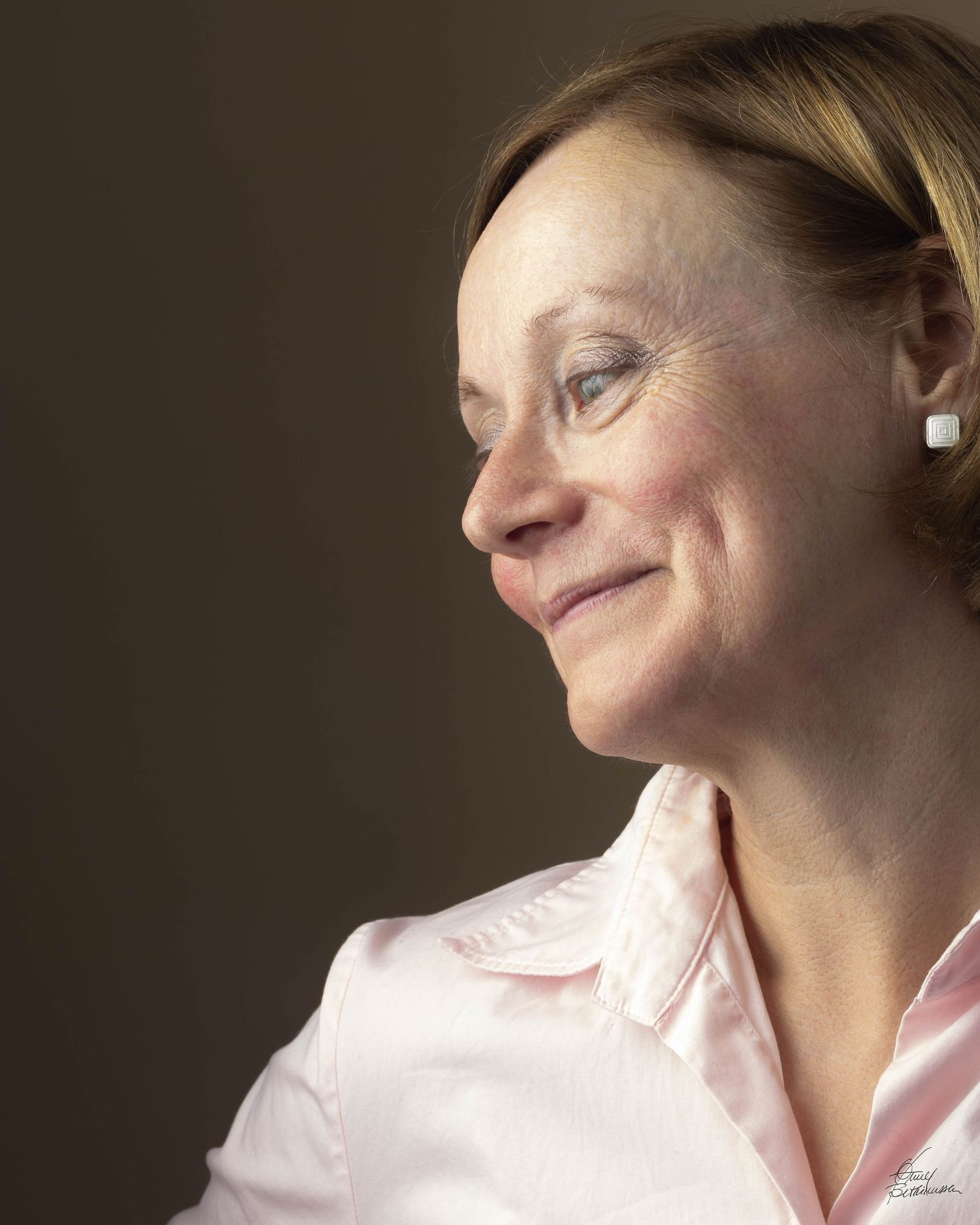 Side profile portrait of person in pink shirt with soft lighting and contemplative expression.