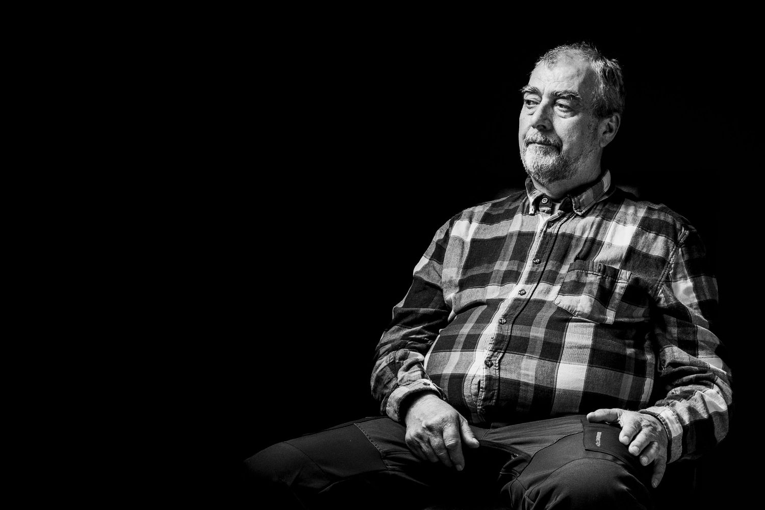 Dramatic black and white portrait showing relaxed pose in checkered shirt.