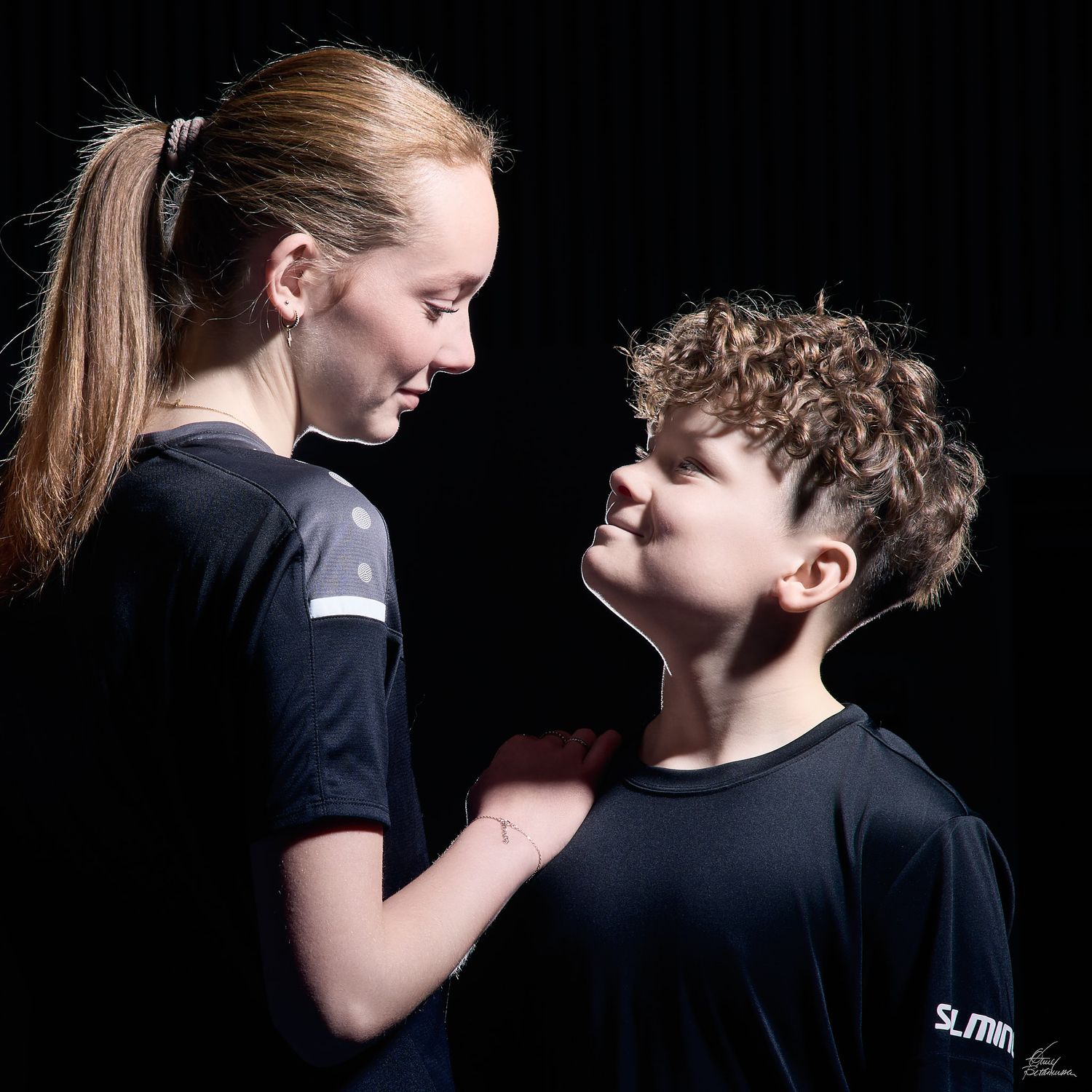 Two young people in black shirts share an intimate moment against a dark background.