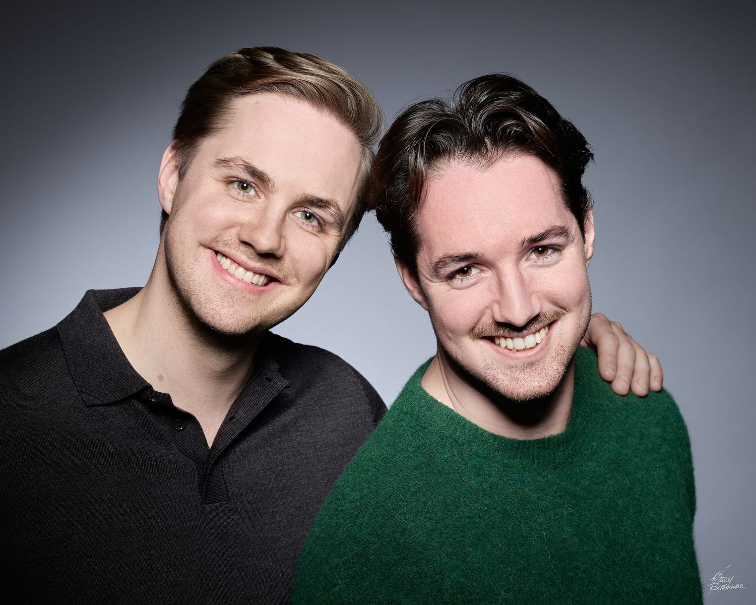 Studio portrait of two people smiling together against grey background.