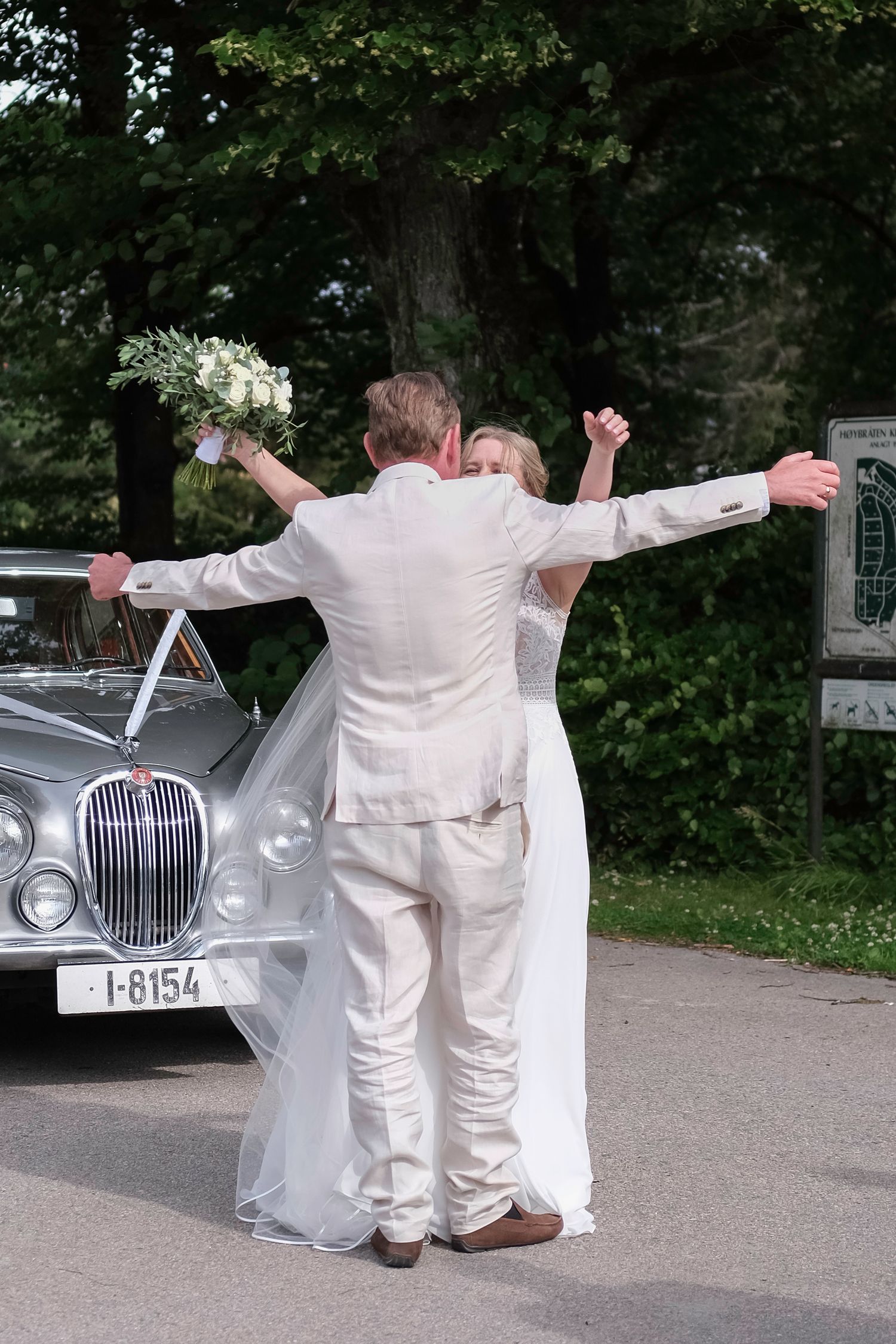 A series of playful poses in front of a classic vintage car during a wedding celebration.