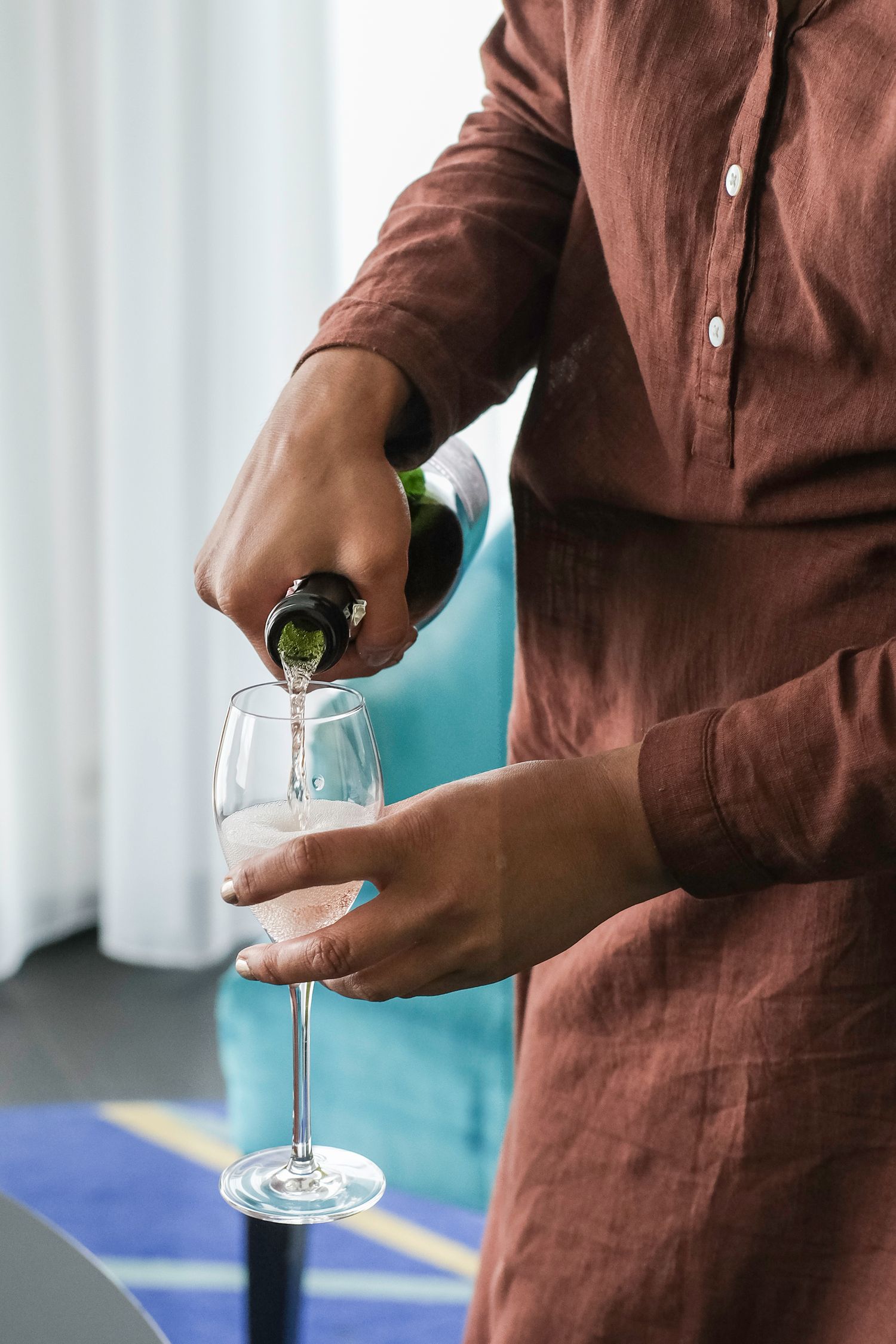 Hands pouring champagne into elegant crystal glasses against a turquoise background.