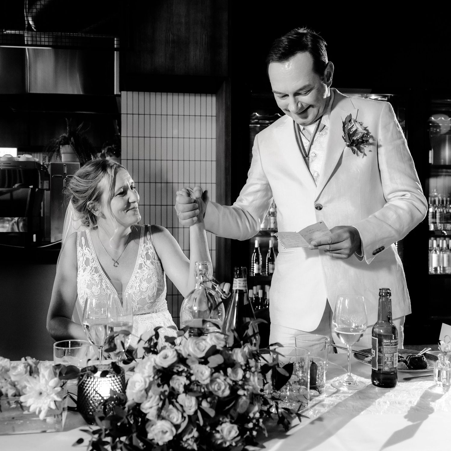 Black and white reception photos showing newlyweds sharing laughs at their wedding dinner table.
