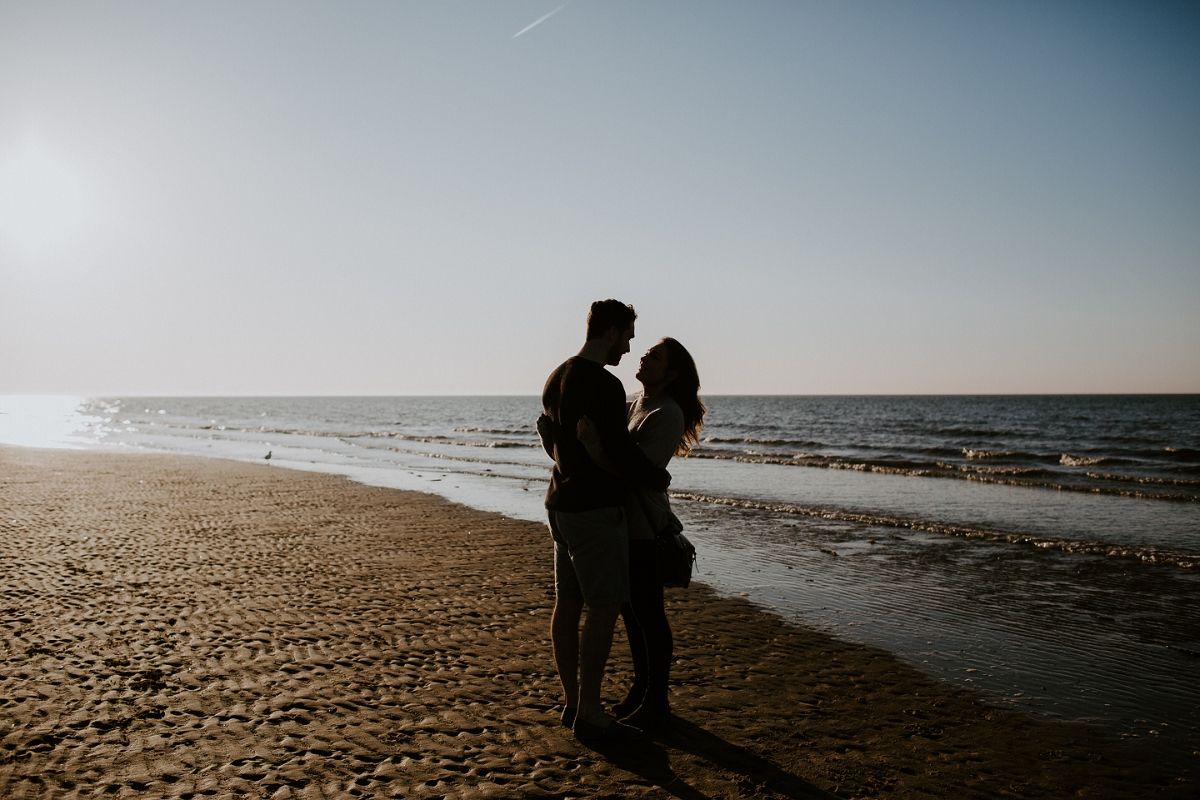 Romantic couple silhouetted against golden sunset on sandy beach near ocean waves.