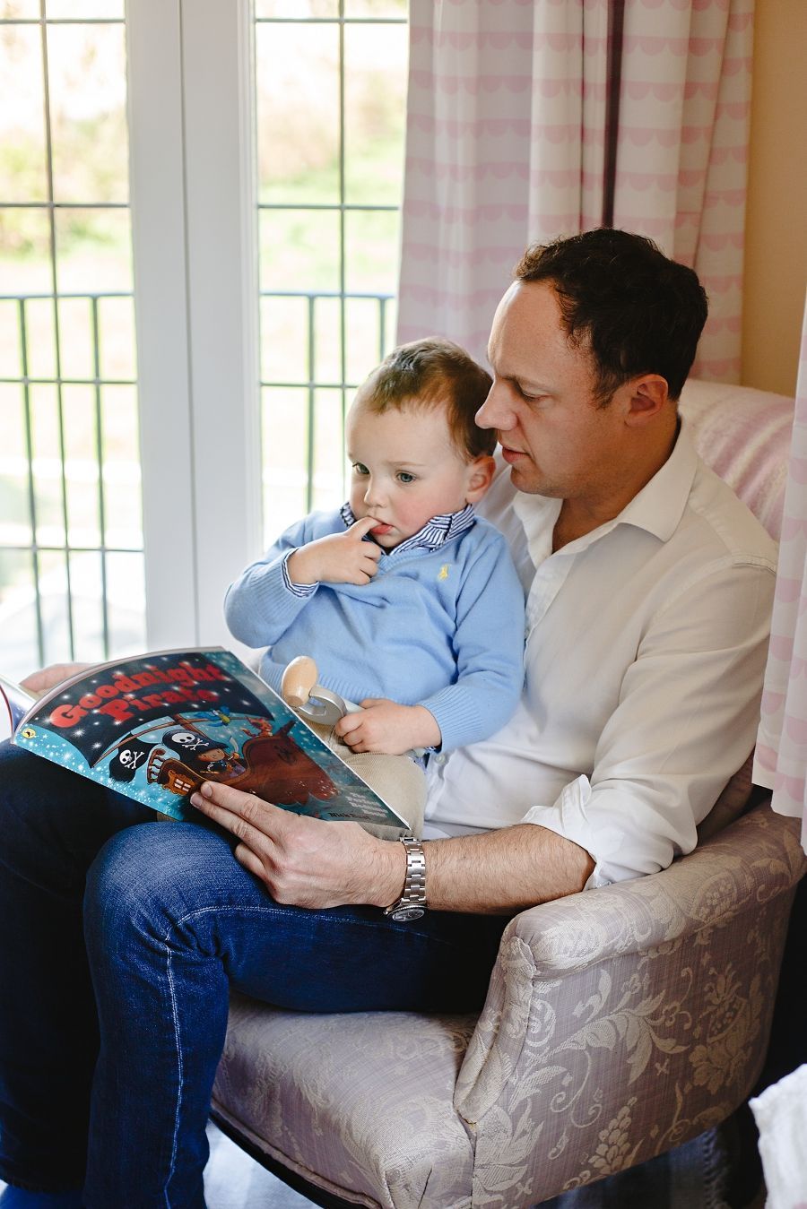 A parent and child share a quiet moment reading a book together in a cosy armchair.