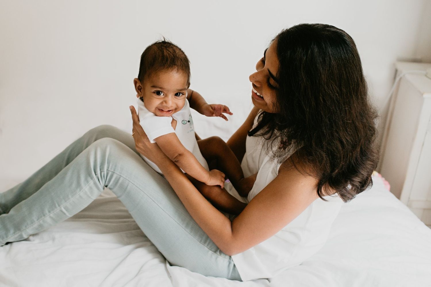 A tender parenting moment captured as they play together on a white bed.