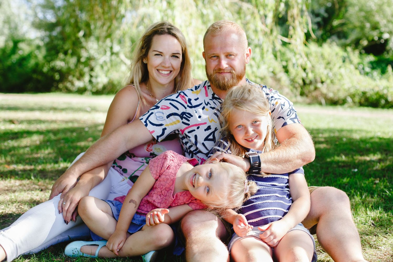 A family sits together on grass in a sunny garden, wearing coordinated blue and pink patterned outfits.